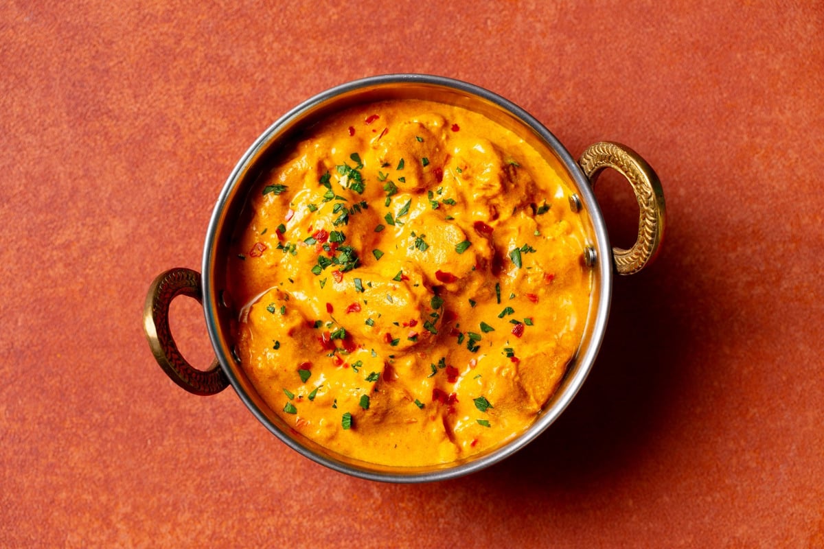 Spicy chicken curry in creamy sauce, served in a traditional bowl. Terracotta-orange background. Close up. Top view.