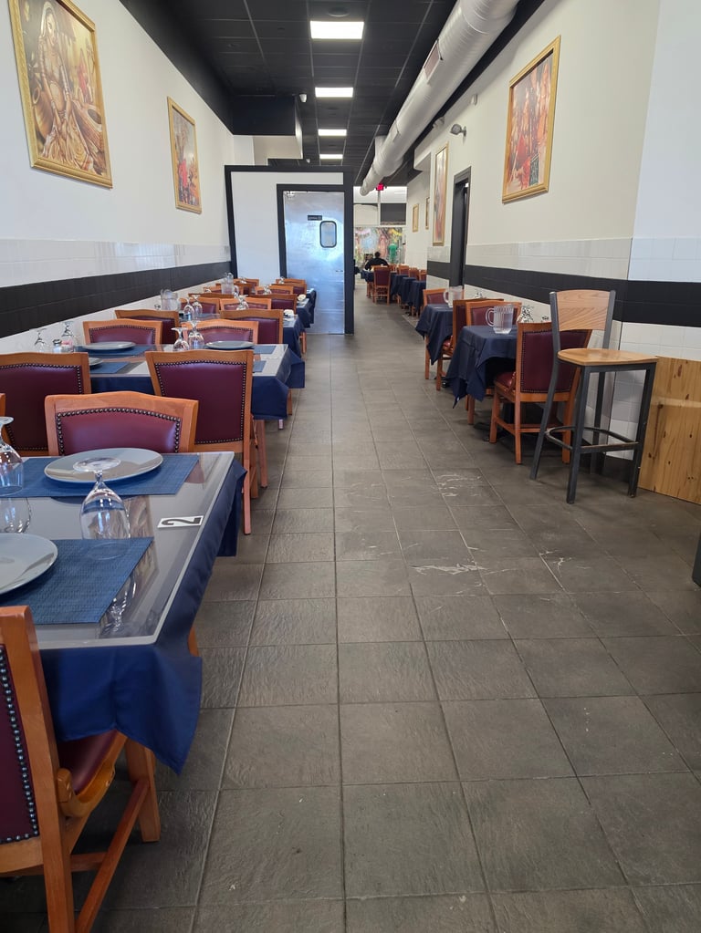 Empty restaurant interior with blue tablecloths, wooden chairs, and place settings along both sides of the dining room.