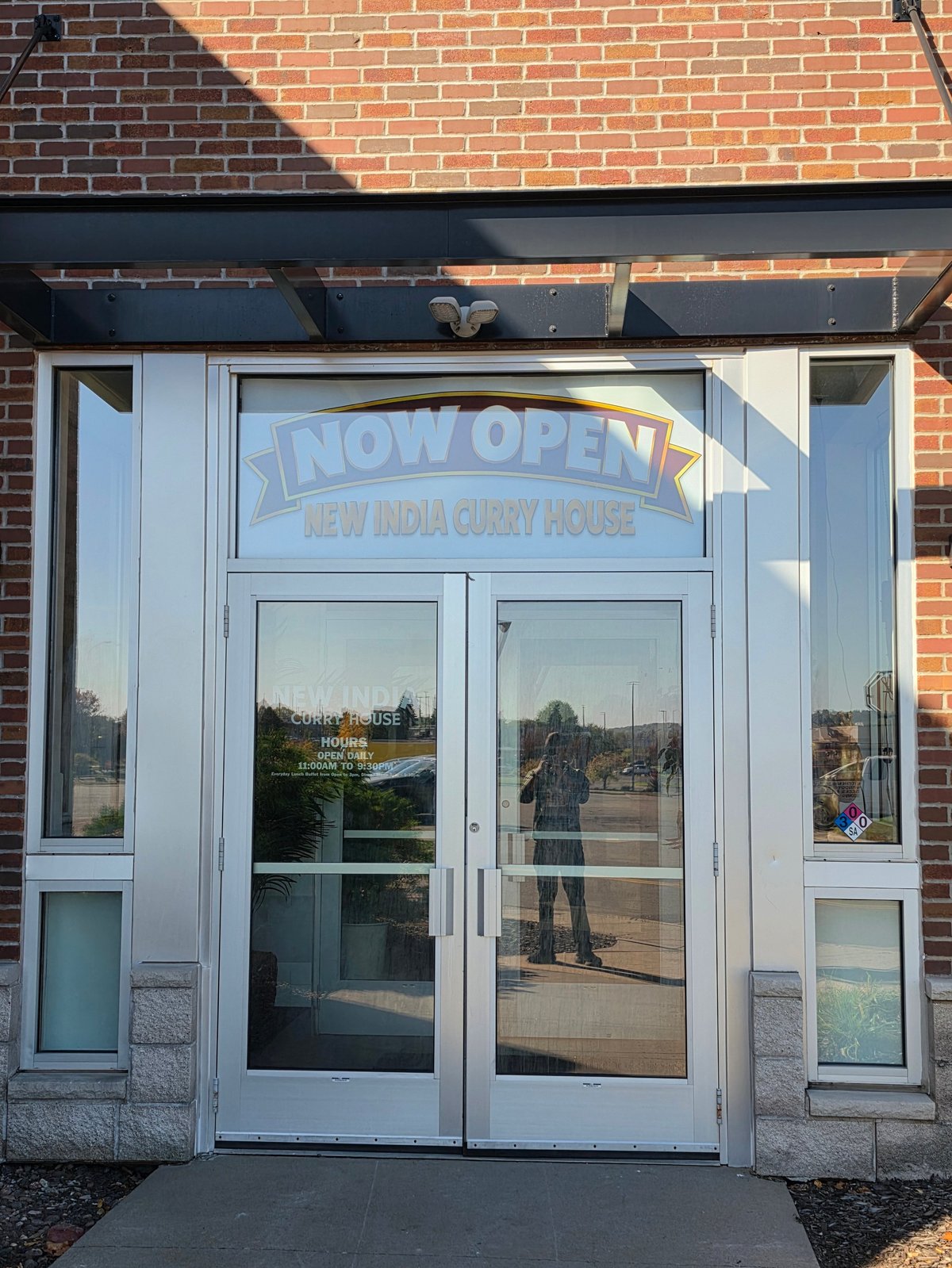 Storefront entrance with white glass doors and Now Open sign for New India Curry House restaurant on brick building