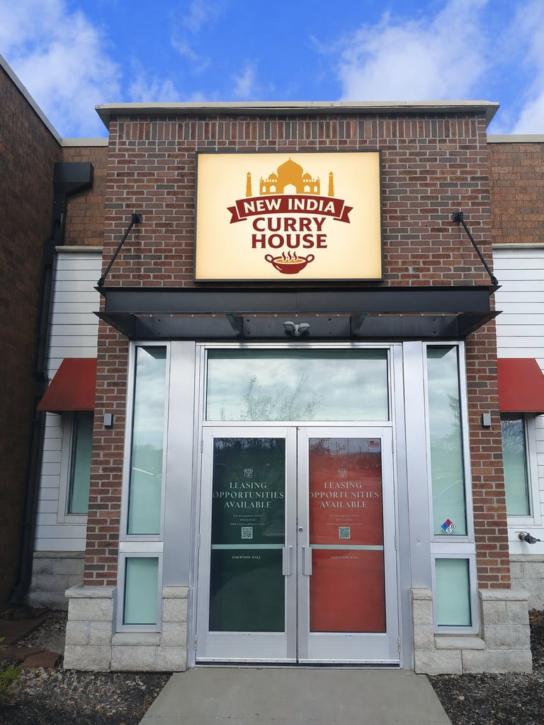 Brick storefront of New India Curry House restaurant with signage above glass doors under blue sky