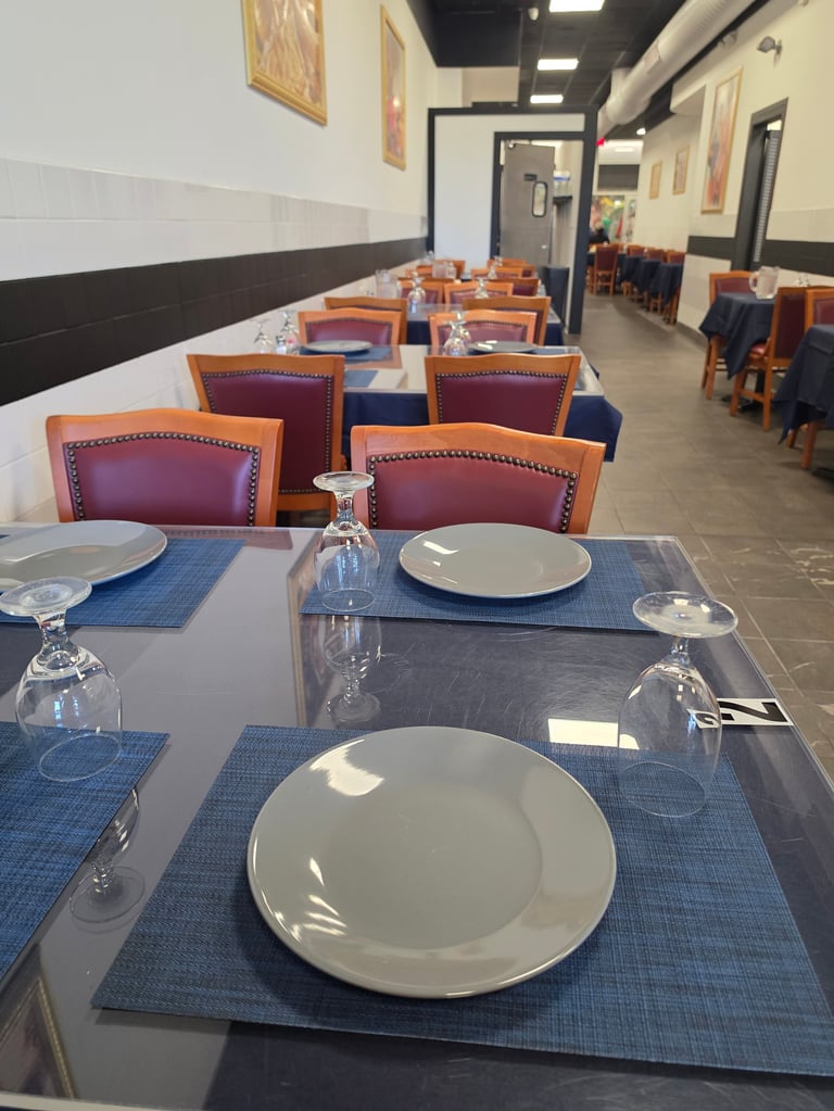 Modern restaurant dining room with rows of tables set with blue placemats, white plates, and glasses, featuring burgundy upholstered chairs with orange wooden frames